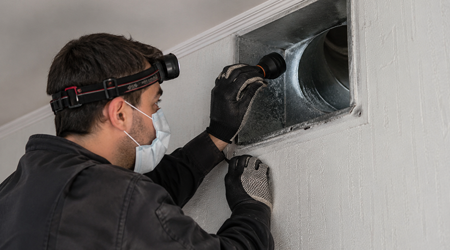 Technician inspecting air duct with flashlight